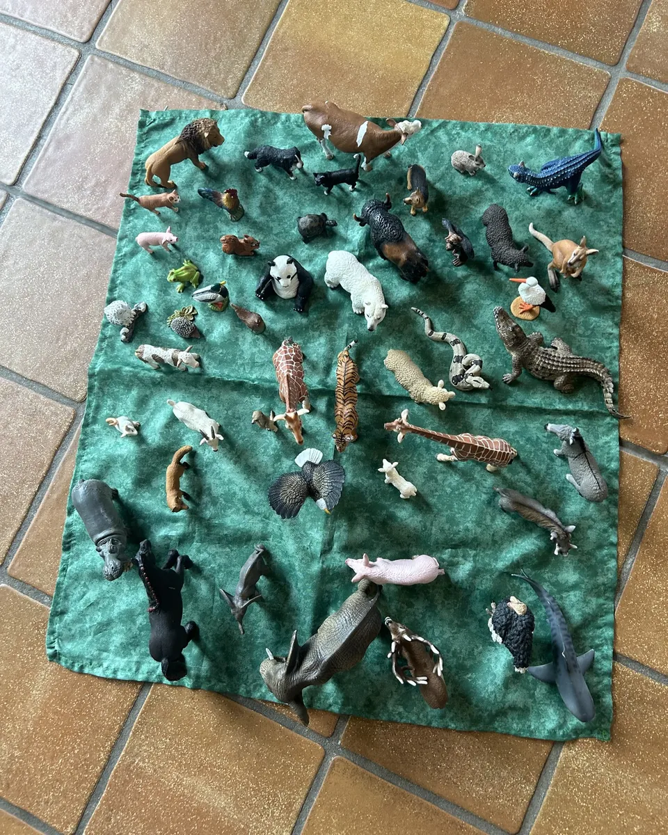 Viele kleine Tierfiguren auf einem grünen Tuch, von oben gesehen
